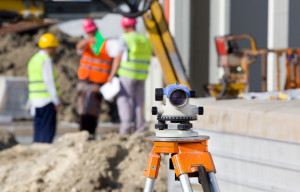 Surveying measuring equipment level theodolite on tripod at construction site with workers in background